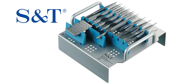 Surgical instrument tray with multiple metal tools arranged in holders. The S&T logo is displayed in the upper left corner.
