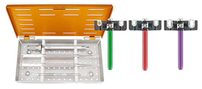 A surgical instrument set with an orange lid contains various tools. Beside it are three surgical instruments with green, red, and purple handles.